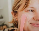 close up of female applying Dandle Organic enzyme mask with manuka honey to cheek with pink applicator