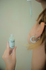 Woman holding a bottle of dandle natural acne spot treatment in one hand and the dropper in the other getting ready to apply to face