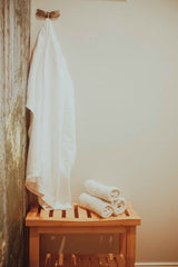 White robe hanging, bamboo chair with white towels rolled and stacked in prenatal massage room in chattanooga, tn at Dandle Spa