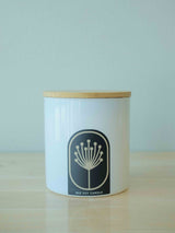 Candle in 9oz white glossy jar with bamboo lid sitting on shelf if local boutique. Hand-poured, non-toxic candle made with soy wax and essential oils. 