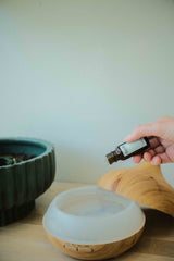 hand holding small glass bottle dropping therapeutic grade essential oils into wooden diffuser. aromatherapy at home. all-natural air freshener 