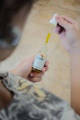 Female holding all-natural antioxidant face oil serum bottle in one hand and dropper in the other. Organic skincare line