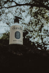 Dandle rosemary mint body lotion bottle on a tree branch with white blossoms in the background. Local Tennessee product. 