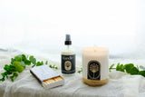 Candle, matches, and  natural room spray on a white surface with green leaves. hand-poured candle made with essential oils. non-toxic candle, all natural room spray, organic linen spray. Locally made Christmas gifts