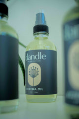 Eczema body oil bottle sitting on surface, front two blurred out, back one clear. Holistic remedy for eczema. Organic body oil