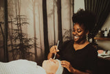Woman performing a facial treatment on another person with a forest background