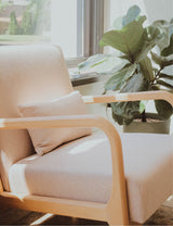 Beige armchair with a pillow next to a potted plant in a room with large windows at Dandle Day Spa where you can get massages, facials, and head spa
