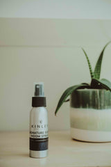 Spray bottle labeled 'KINLEY hotel' on a wooden surface with a plant in the background